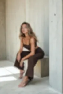 Hnědé tencelové dámské pyžamo s dlouhými kalhotami a topem na ramínka, focené u betonové stěny.