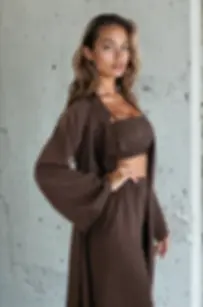 Hnědé tencelové dámské pyžamo s dlouhým topem, širokými rukávy a kalhotami, focené u betonové stěny.