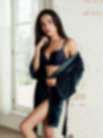 Tmavě zelený sametový župan s dlouhými rukávy, focený u okna na modelce v černém prádle.