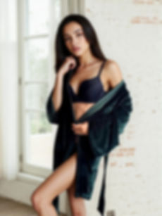 Tmavě zelený sametový župan s dlouhými rukávy, focený u okna na modelce v černém prádle.