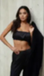 Černé hedvábné dámské pyžamo s topem na ramínka a volnými kalhotami, focené na modelce u betonové stěny.