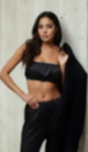 Černé hedvábné dámské pyžamo s topem na ramínka a volnými kalhotami, focené na modelce u betonové stěny.